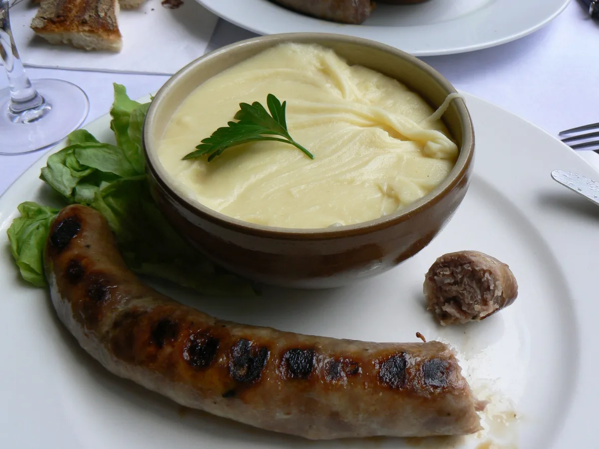 Aligot filant servi dans un bol, accompagné d'une saucisse grillée