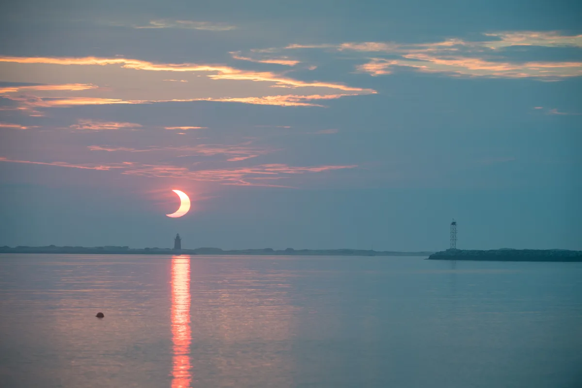 Éclipse solaire partielle avec le Soleil bas sur l'horizon, en silhouette derrière un phare