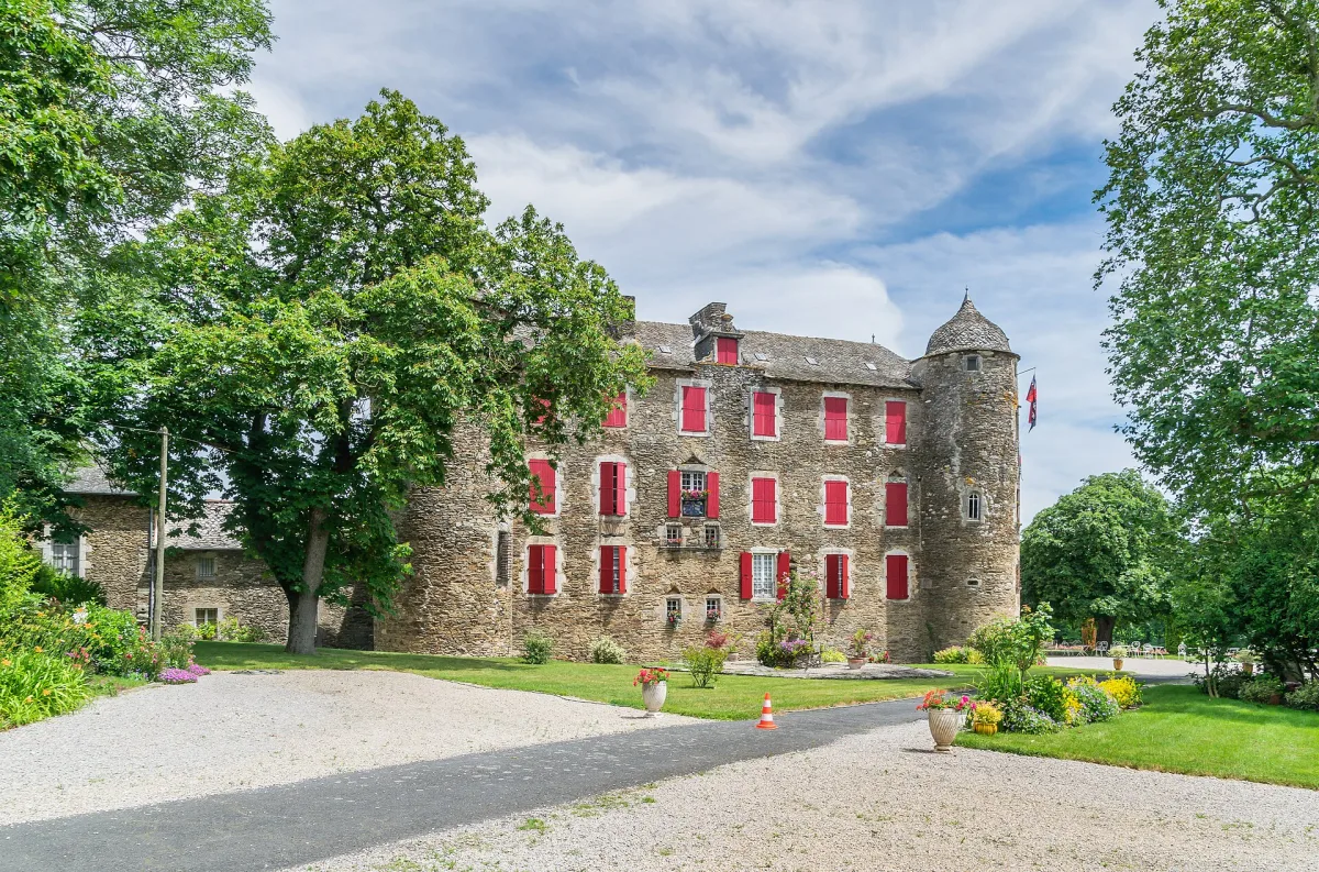 Façade en pierre du château du Bosc à Camjac avec ses tourelles rondes et son parc arboré
