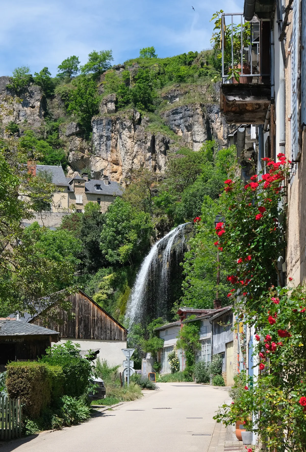 Cascade de Salles-la-Source dévalant la falaise calcaire au-dessus des toits du village, Aveyron