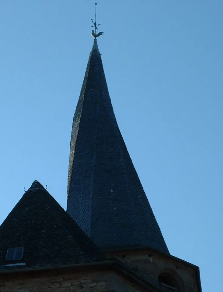 Le clocher tors flamboyant de l'église Notre-Dame-de-l'Assomption de Saint-Côme-d'Olt, en pierre de lave vrillée, dominant les toits du village médiéval